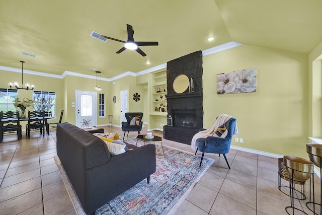 tiled living room featuring ornamental molding, a stone fireplace, ceiling fan with notable chandelier, and built in features