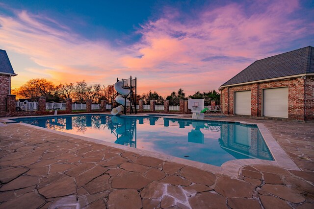 pool at dusk featuring a water slide and a patio