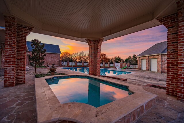 pool at dusk with a patio area and a hot tub