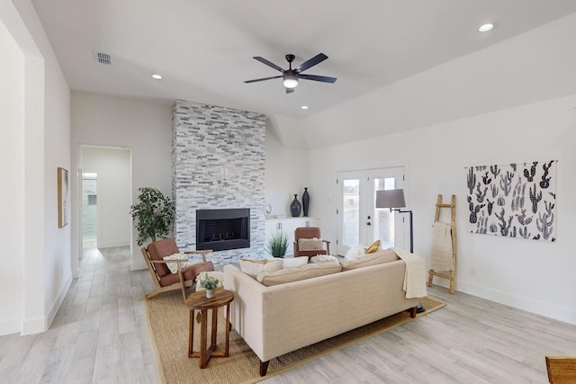 living room featuring ceiling fan, french doors, a stone fireplace, light hardwood / wood-style flooring, and vaulted ceiling