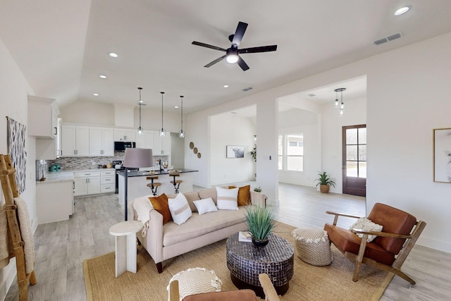 living room with ceiling fan, light hardwood / wood-style flooring, and vaulted ceiling