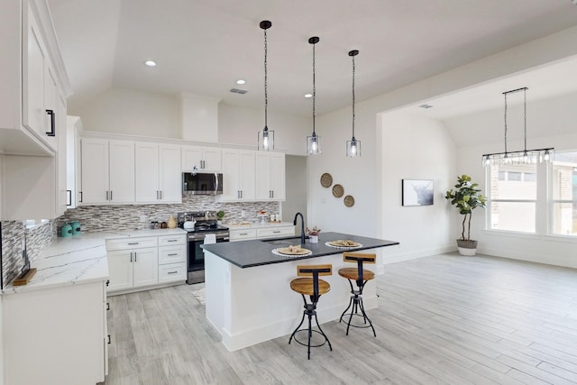 kitchen with sink, lofted ceiling, a kitchen island with sink, white cabinets, and appliances with stainless steel finishes