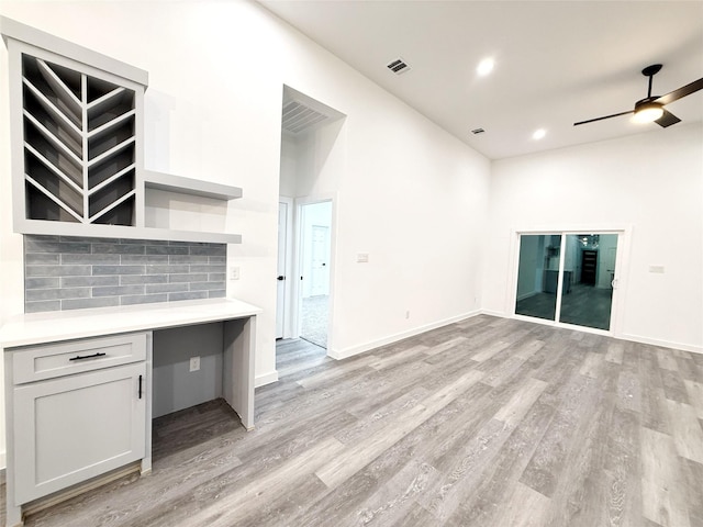 kitchen with light wood-type flooring, built in desk, ceiling fan, and backsplash