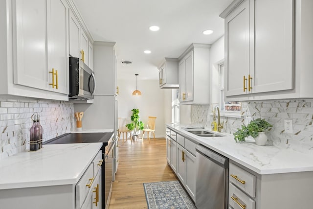 kitchen featuring sink, stainless steel appliances, light stone counters, decorative light fixtures, and light wood-type flooring