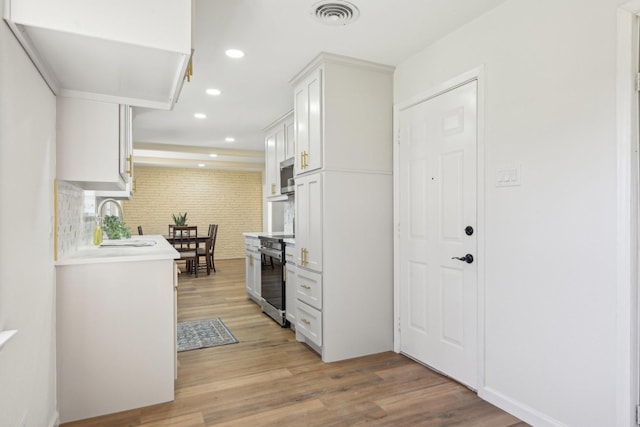 kitchen featuring backsplash, light wood-type flooring, stainless steel appliances, sink, and white cabinetry