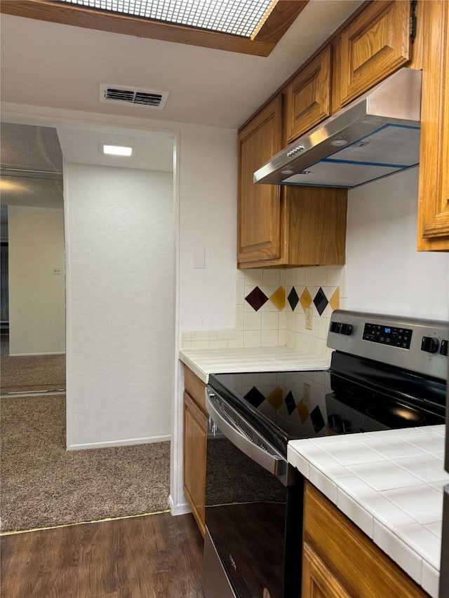 kitchen with tile countertops, stainless steel electric range, dark wood-type flooring, exhaust hood, and decorative backsplash