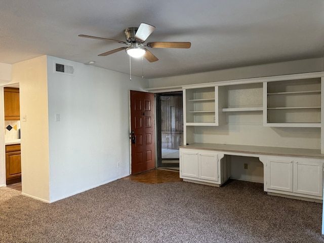 unfurnished office featuring ceiling fan, dark carpet, built in study area, and visible vents