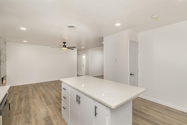 kitchen featuring a center island, white cabinets, light hardwood / wood-style flooring, ceiling fan, and light stone countertops