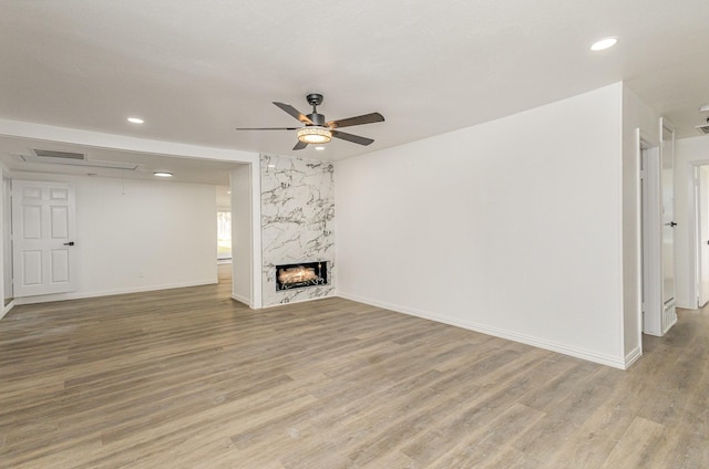 unfurnished living room with ceiling fan, a premium fireplace, and light hardwood / wood-style flooring