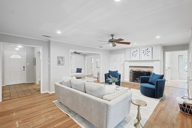 living room featuring a fireplace, light hardwood / wood-style floors, ceiling fan, and crown molding