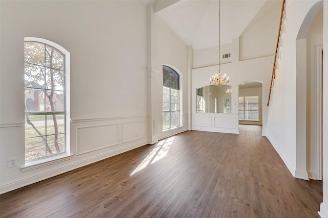 unfurnished dining area with an inviting chandelier, high vaulted ceiling, and dark wood-type flooring