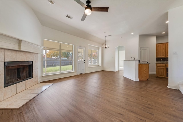 unfurnished living room featuring a tiled fireplace, ceiling fan with notable chandelier, and dark hardwood / wood-style flooring