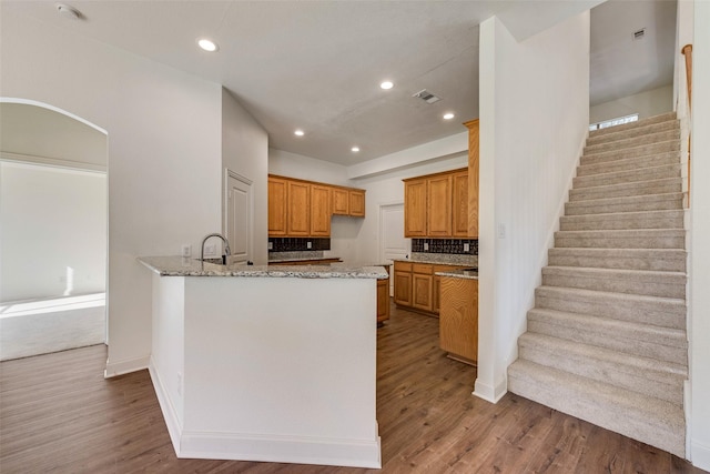 kitchen featuring sink, wood-type flooring, light stone countertops, and kitchen peninsula