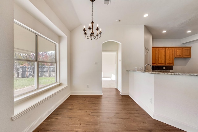 unfurnished dining area with an inviting chandelier, sink, dark wood-type flooring, and lofted ceiling