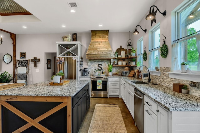 kitchen with stainless steel appliances, light stone counters, premium range hood, and sink