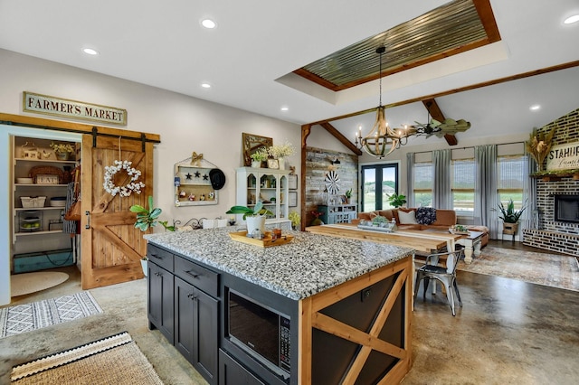 kitchen with light stone countertops, built in microwave, pendant lighting, a barn door, and a kitchen island