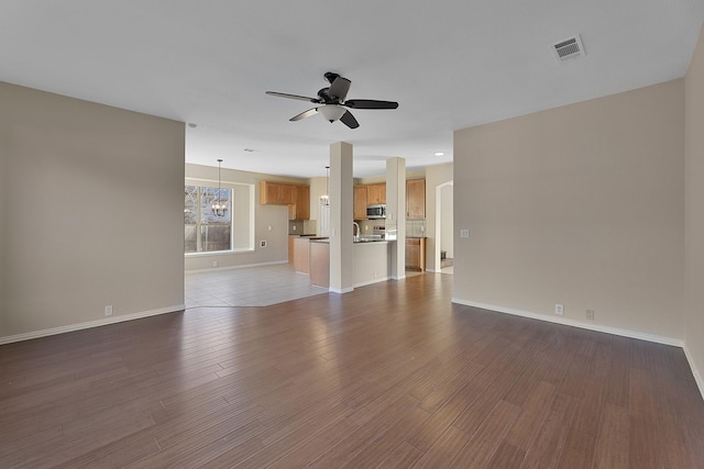 unfurnished living room with ceiling fan with notable chandelier and dark wood-type flooring