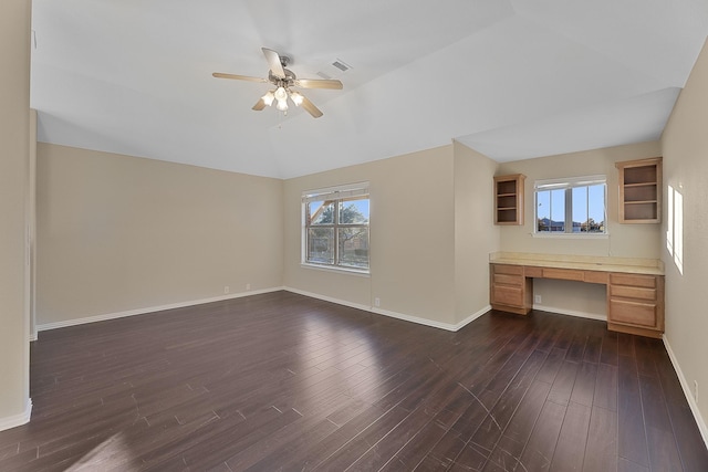 unfurnished living room with ceiling fan, built in desk, dark wood-type flooring, and vaulted ceiling