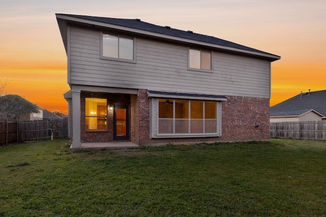 back house at dusk with a lawn and a patio