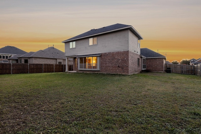 back house at dusk featuring a lawn