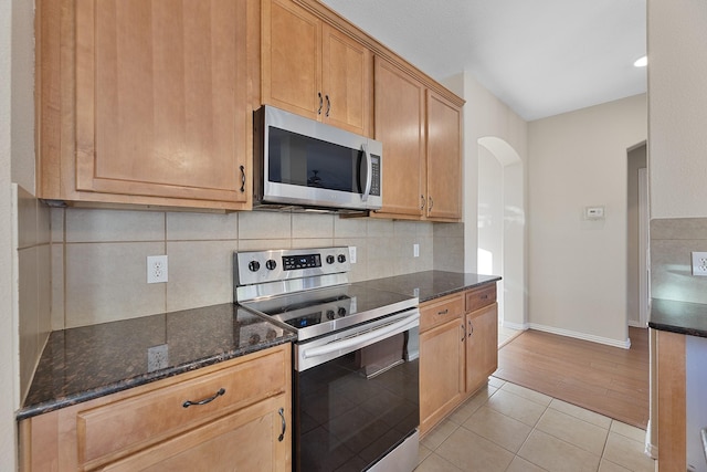 kitchen with light hardwood / wood-style floors, tasteful backsplash, appliances with stainless steel finishes, and dark stone counters