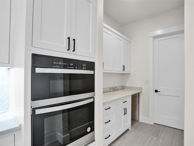 kitchen with light stone counters, white cabinets, and stainless steel double oven