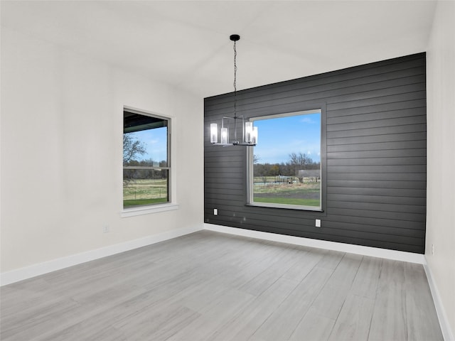 unfurnished dining area featuring wooden walls, light hardwood / wood-style flooring, and a chandelier