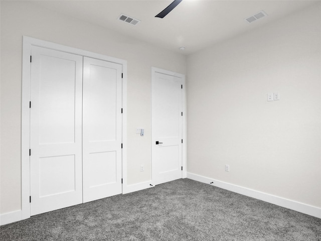 unfurnished bedroom with ceiling fan, dark carpet, and a closet