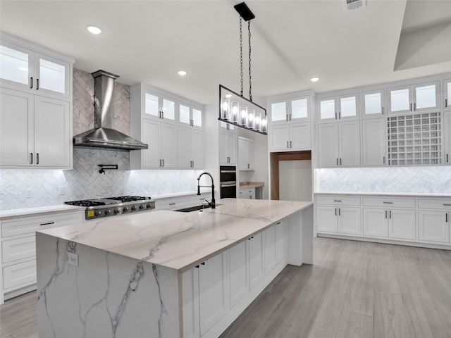 kitchen featuring white cabinetry, a spacious island, wall chimney range hood, and sink