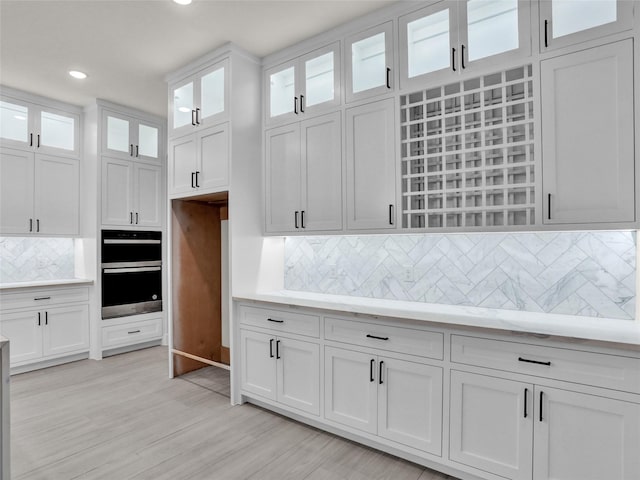 kitchen with white cabinets, decorative backsplash, stainless steel double oven, and light hardwood / wood-style flooring