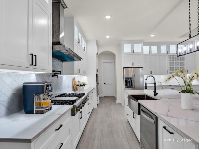 kitchen featuring appliances with stainless steel finishes, light stone counters, wall chimney range hood, pendant lighting, and white cabinetry