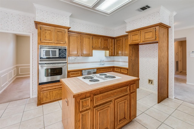 kitchen with a kitchen island, tile countertops, light tile patterned floors, stainless steel appliances, and crown molding