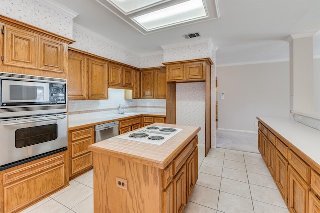 kitchen with light tile patterned floors, sink, appliances with stainless steel finishes, a center island, and ornamental molding