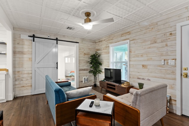 living room featuring a barn door, dark wood-type flooring, ceiling fan, and wooden walls