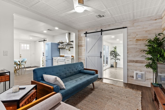 living room with hardwood / wood-style floors, a barn door, ceiling fan, and wooden walls