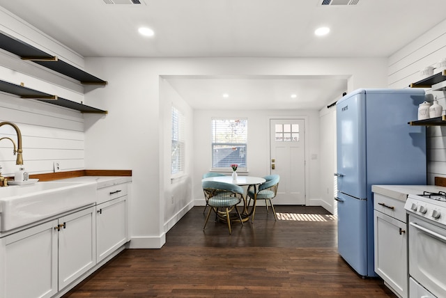 kitchen with white stove, sink, white cabinetry, and dark wood-type flooring