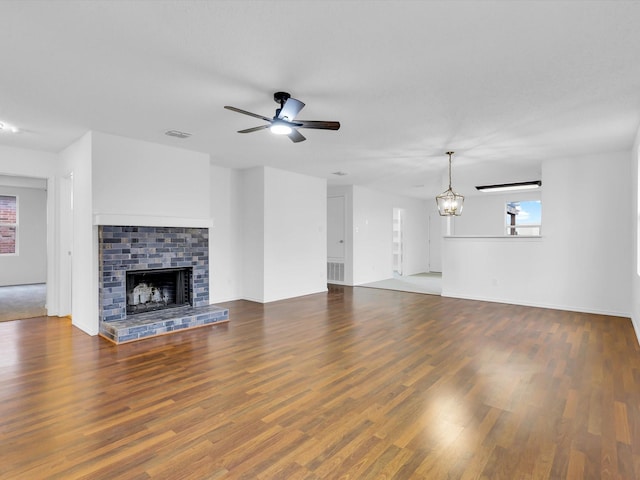 unfurnished living room featuring dark hardwood / wood-style floors, ceiling fan with notable chandelier, and a brick fireplace