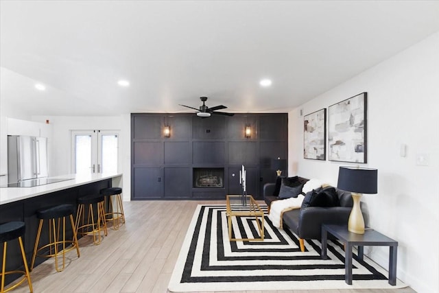 living room featuring ceiling fan, light hardwood / wood-style floors, a fireplace, and french doors