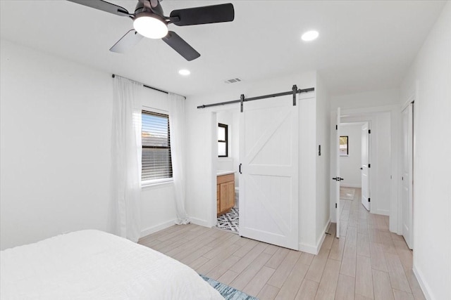 bedroom with ceiling fan, a barn door, light hardwood / wood-style flooring, and ensuite bath