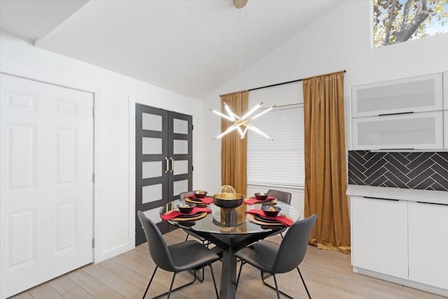 dining area with a chandelier, light wood-type flooring, and vaulted ceiling