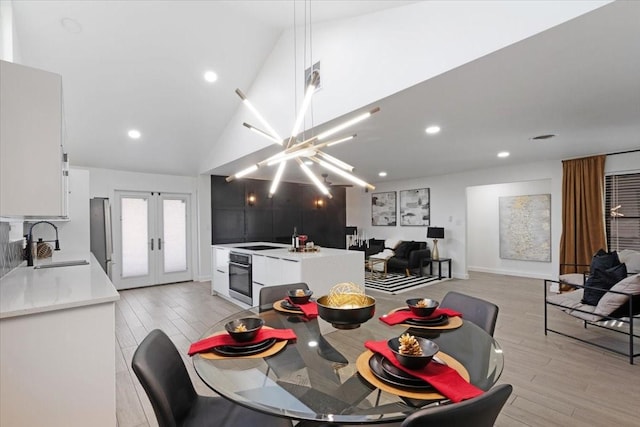 dining space featuring sink, high vaulted ceiling, light hardwood / wood-style floors, and french doors