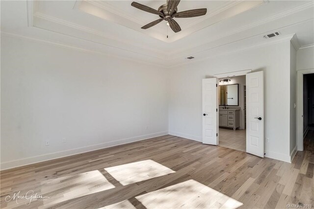 unfurnished bedroom with ceiling fan, a raised ceiling, crown molding, and light hardwood / wood-style flooring