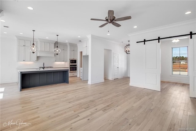 kitchen featuring a barn door, light hardwood / wood-style flooring, an island with sink, pendant lighting, and white cabinets