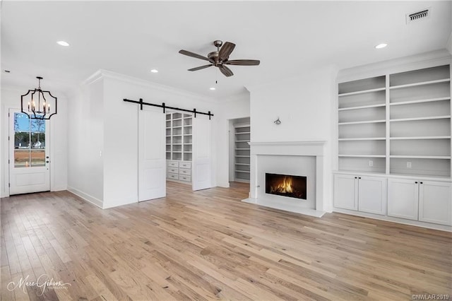 unfurnished living room with ceiling fan with notable chandelier, light hardwood / wood-style floors, a barn door, and crown molding