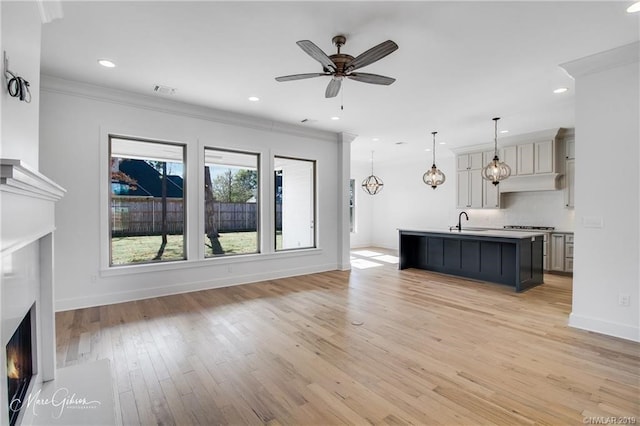 unfurnished living room featuring ceiling fan with notable chandelier, light wood-type flooring, ornamental molding, and sink