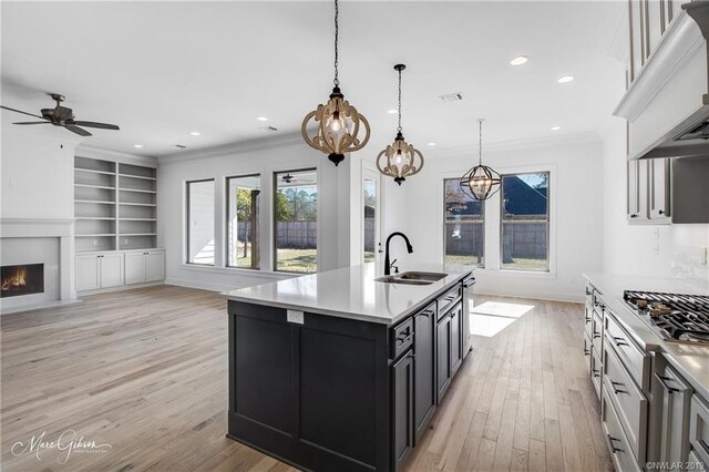 kitchen with sink, light hardwood / wood-style flooring, decorative light fixtures, a kitchen island with sink, and custom exhaust hood