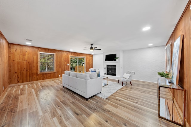 living room with a large fireplace, wooden walls, light hardwood / wood-style flooring, and ceiling fan