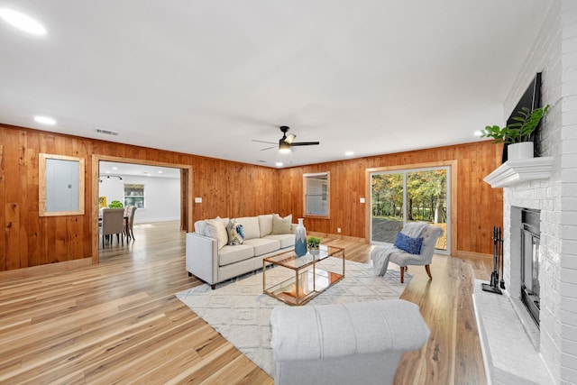 living room featuring wooden walls, a fireplace, ceiling fan, and light wood-type flooring