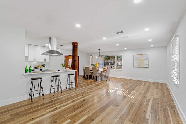 kitchen with light hardwood / wood-style flooring, kitchen peninsula, pendant lighting, white cabinets, and exhaust hood