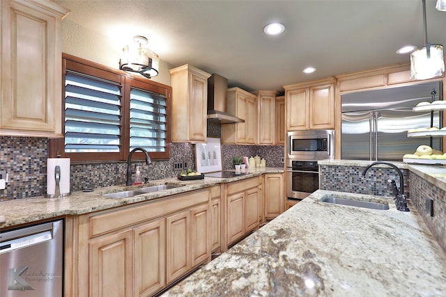 kitchen featuring built in appliances, wall chimney exhaust hood, sink, and hanging light fixtures